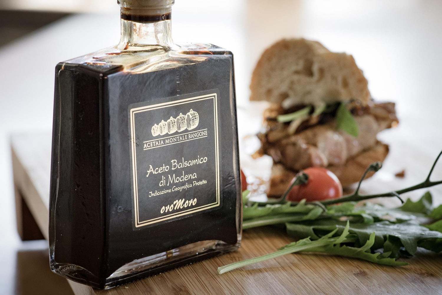 Aceto Balsamico Flasche auf Tisch mit Tomaten, Kräutern und Brot
